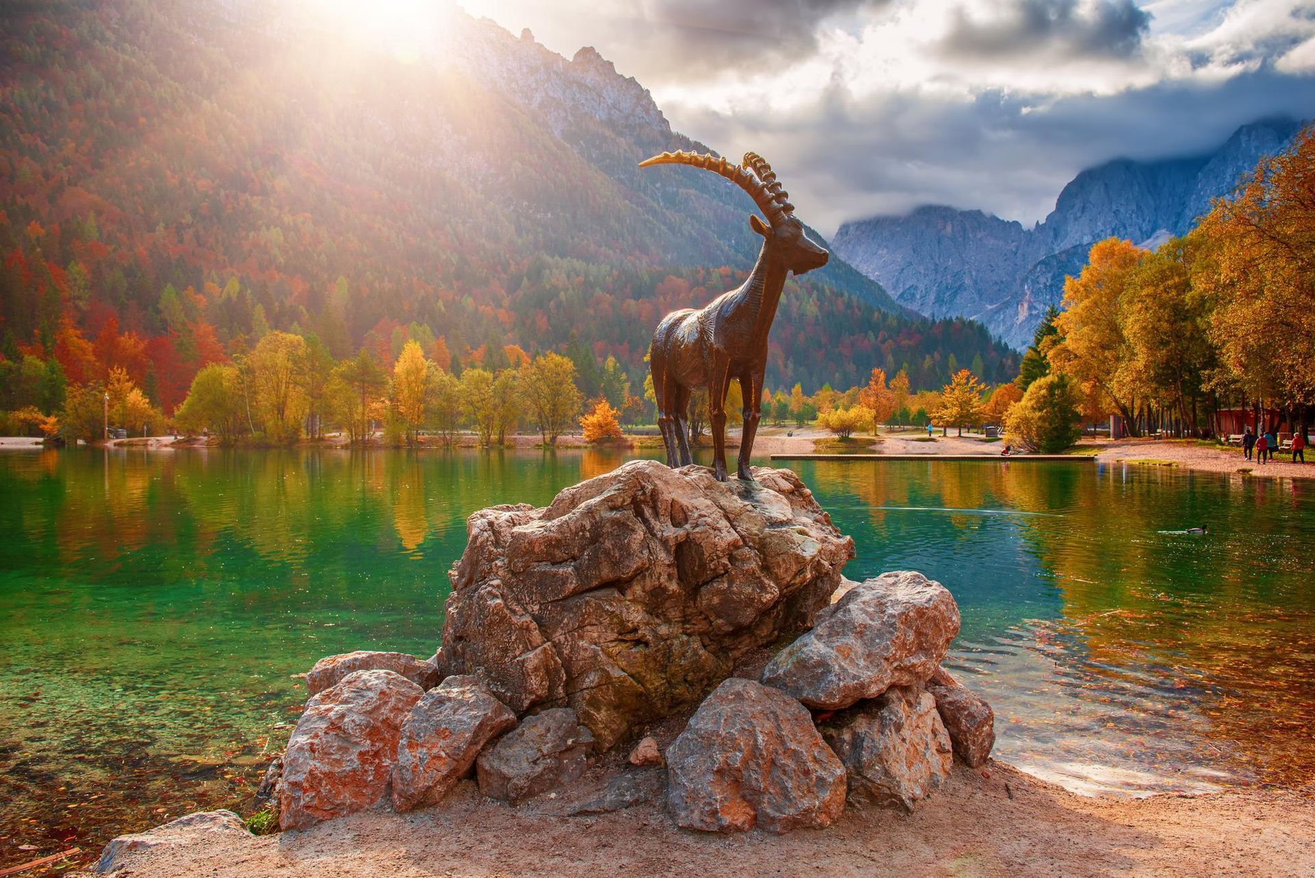 A statue of a goat standing on top of a rock next to a lake.