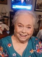 A woman is smiling in front of a television in a living room.