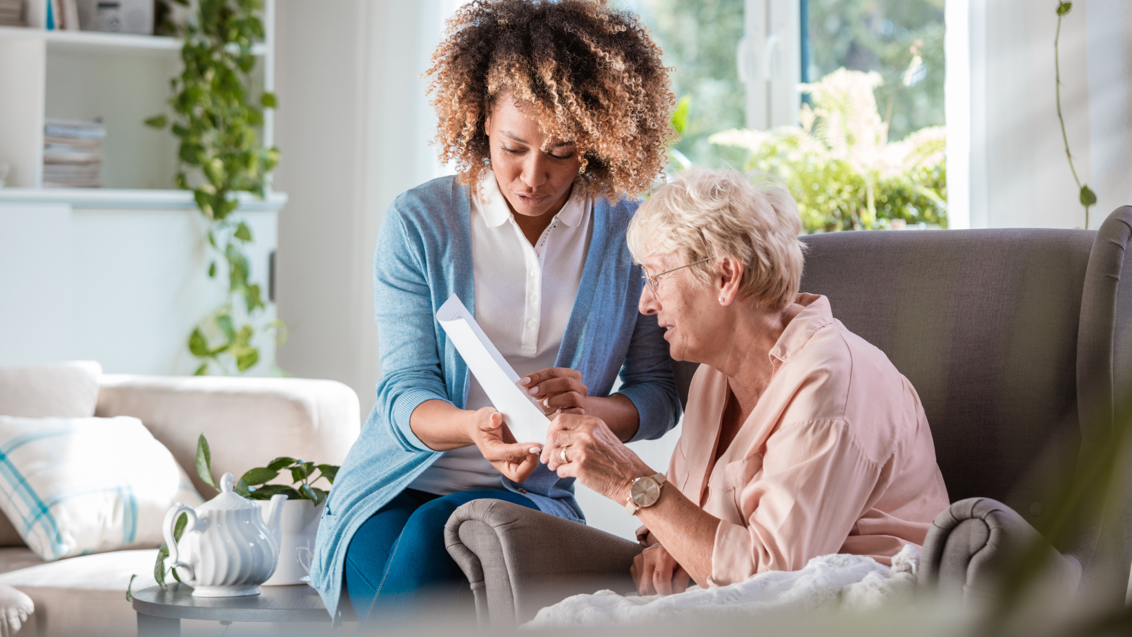 A woman is sitting next to an older woman on a couch looking at a piece of paper.