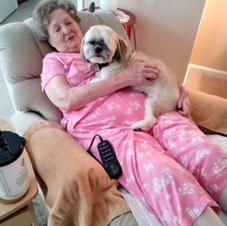 An elderly woman is sitting in a chair holding a small dog.