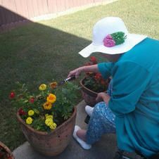 A woman is kneeling down in front of a potted plant with flowers.