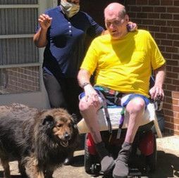 A man in a wheelchair is standing next to a dog.