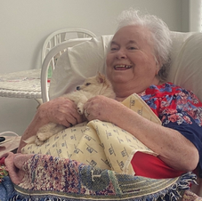 An elderly woman is sitting in a chair holding a dog
