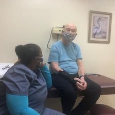 A man wearing a mask is sitting on a table with a nurse.