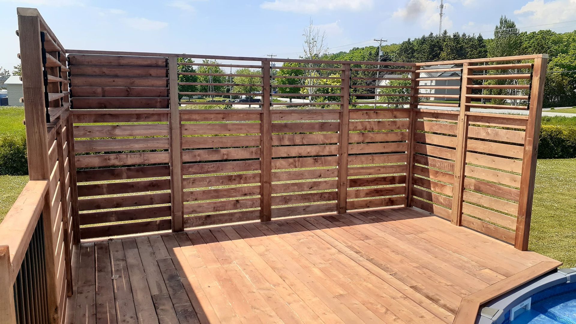 Une terrasse en bois avec une clôture autour et une piscine en arrière-plan.