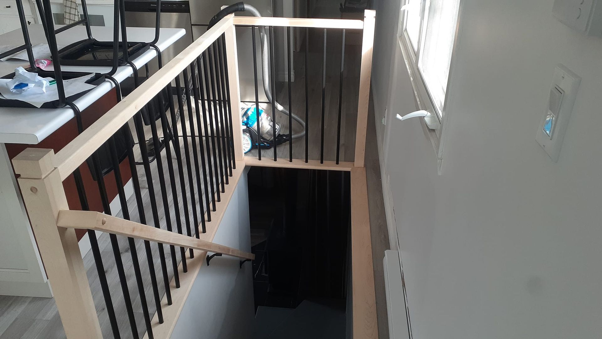Un escalier en bois avec une rampe noire monte au deuxième étage d'une maison.