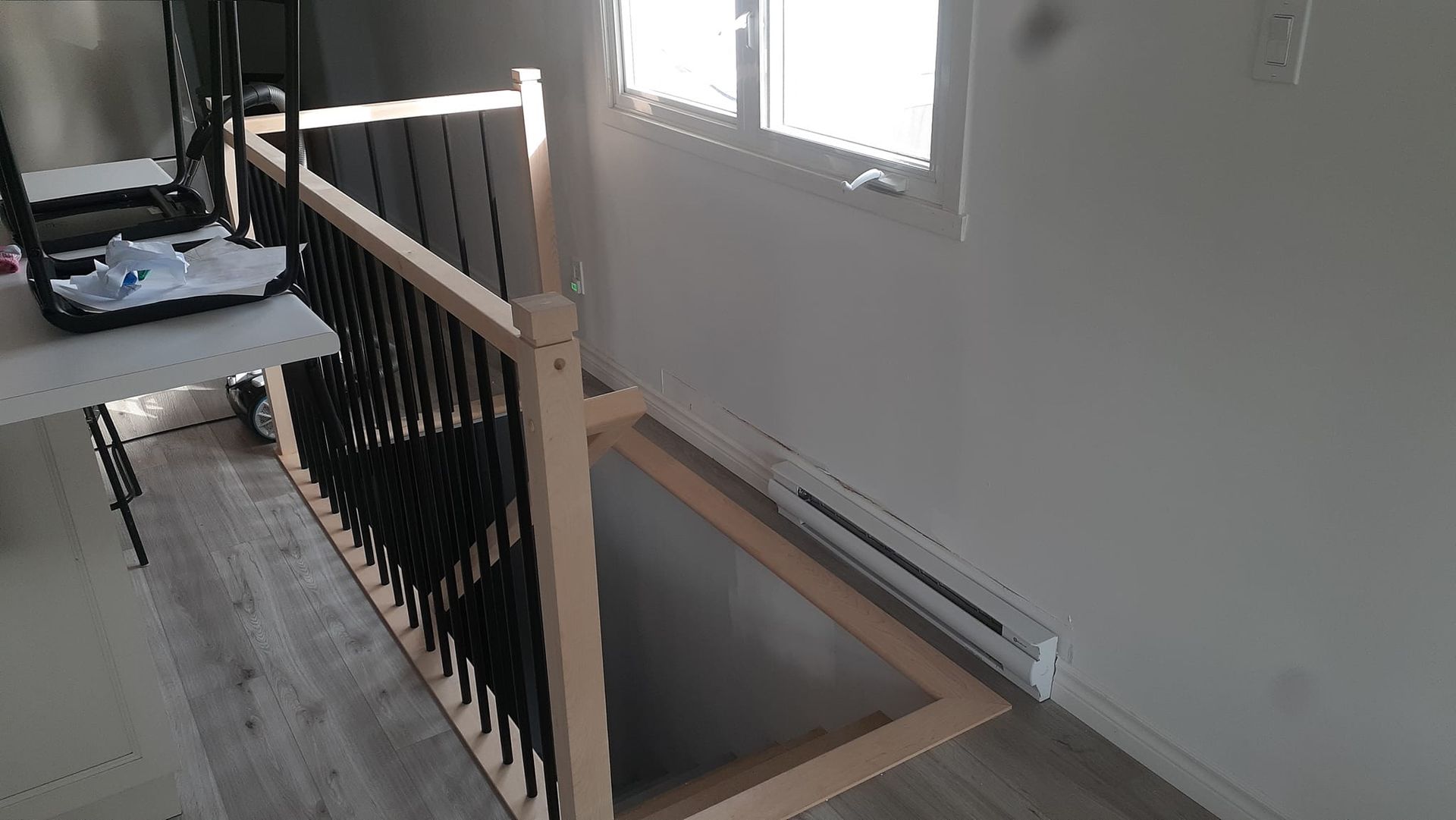 Un escalier en bois avec une rampe noire dans une pièce à côté d'une fenêtre.