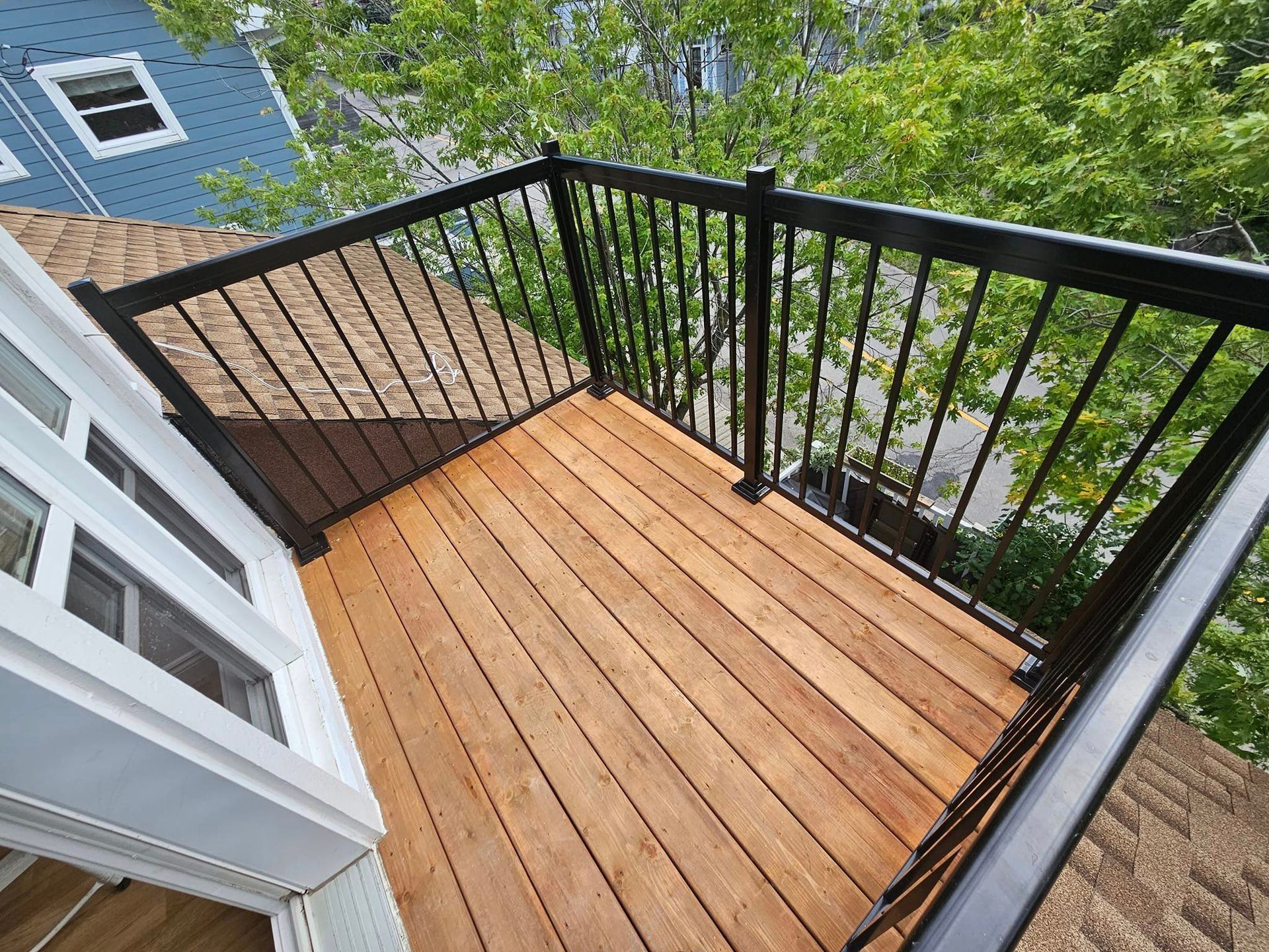 Un balcon avec une terrasse en bois et une balustrade noire.