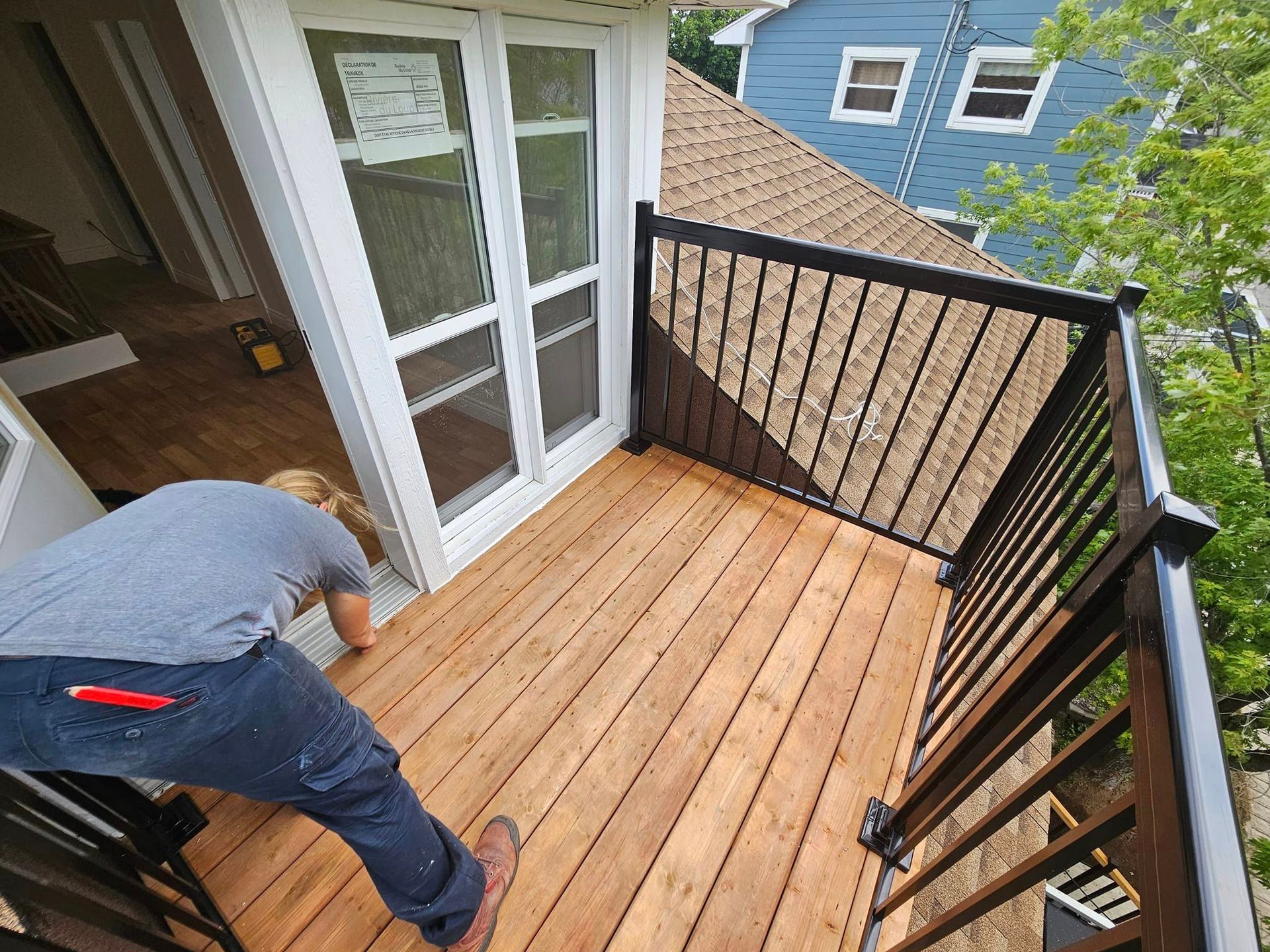 Un homme travaille sur une terrasse en bois avec une balustrade noire.