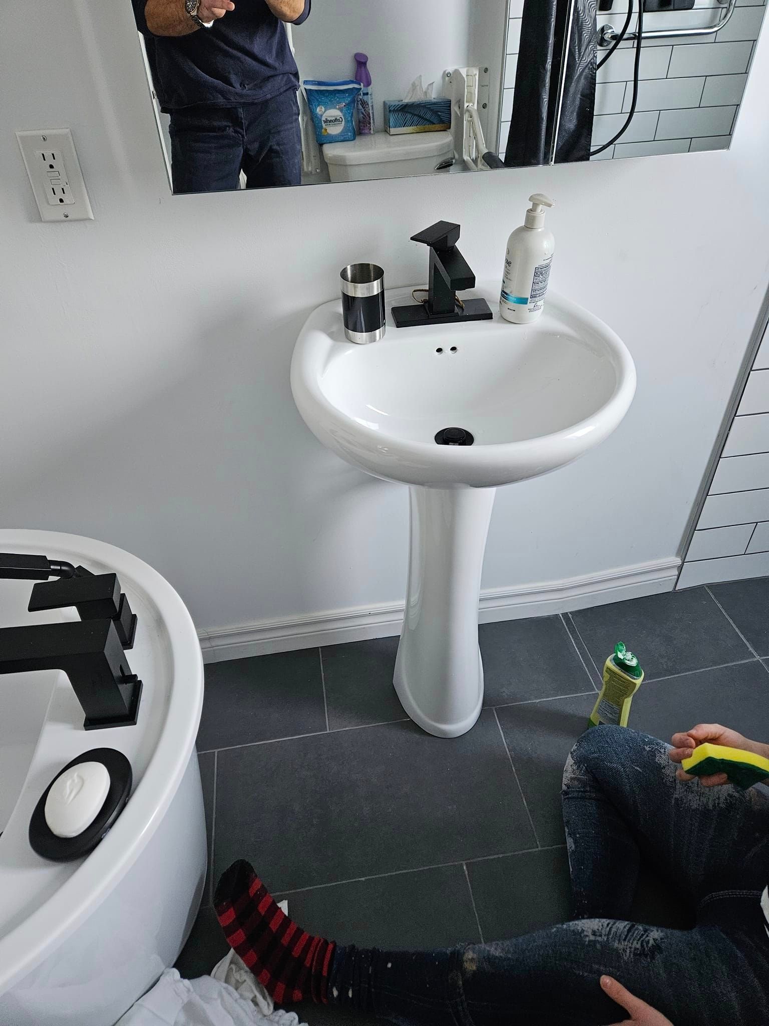 Une personne est assise dans une salle de bain à côté d'un lavabo.