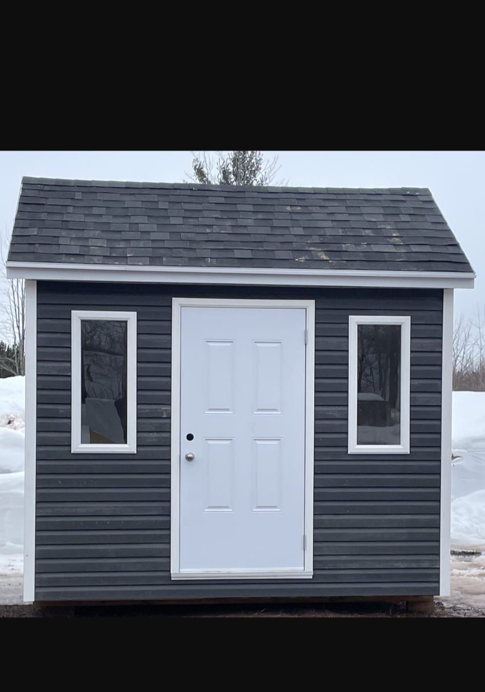 Un petit hangar avec une porte et des fenêtres blanches est assis dans la neige.