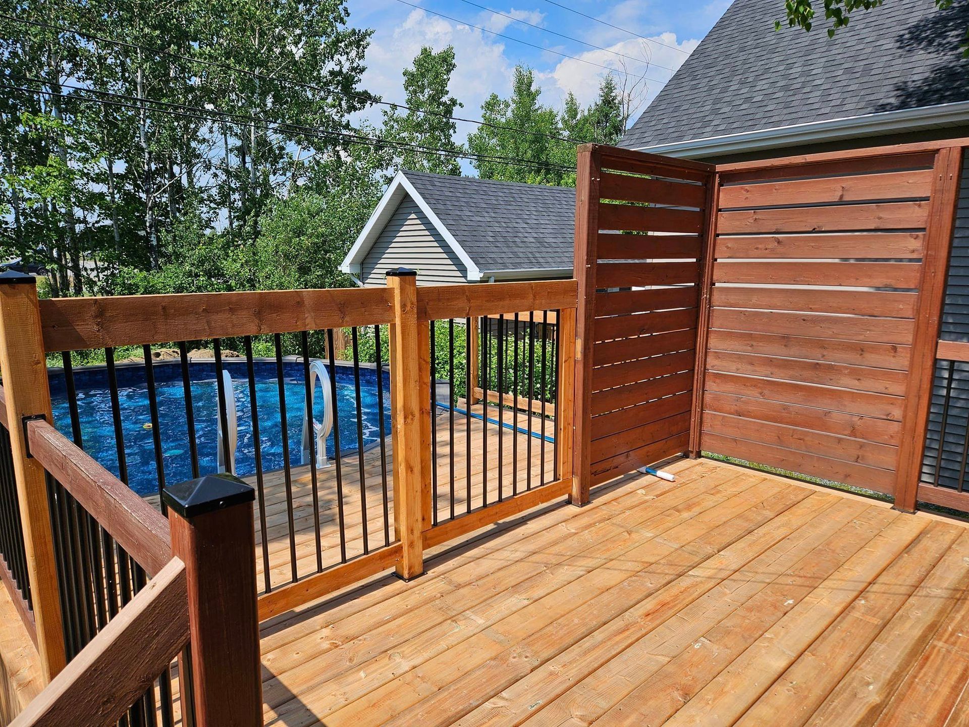 Une terrasse en bois avec une clôture et une piscine en arrière-plan.
