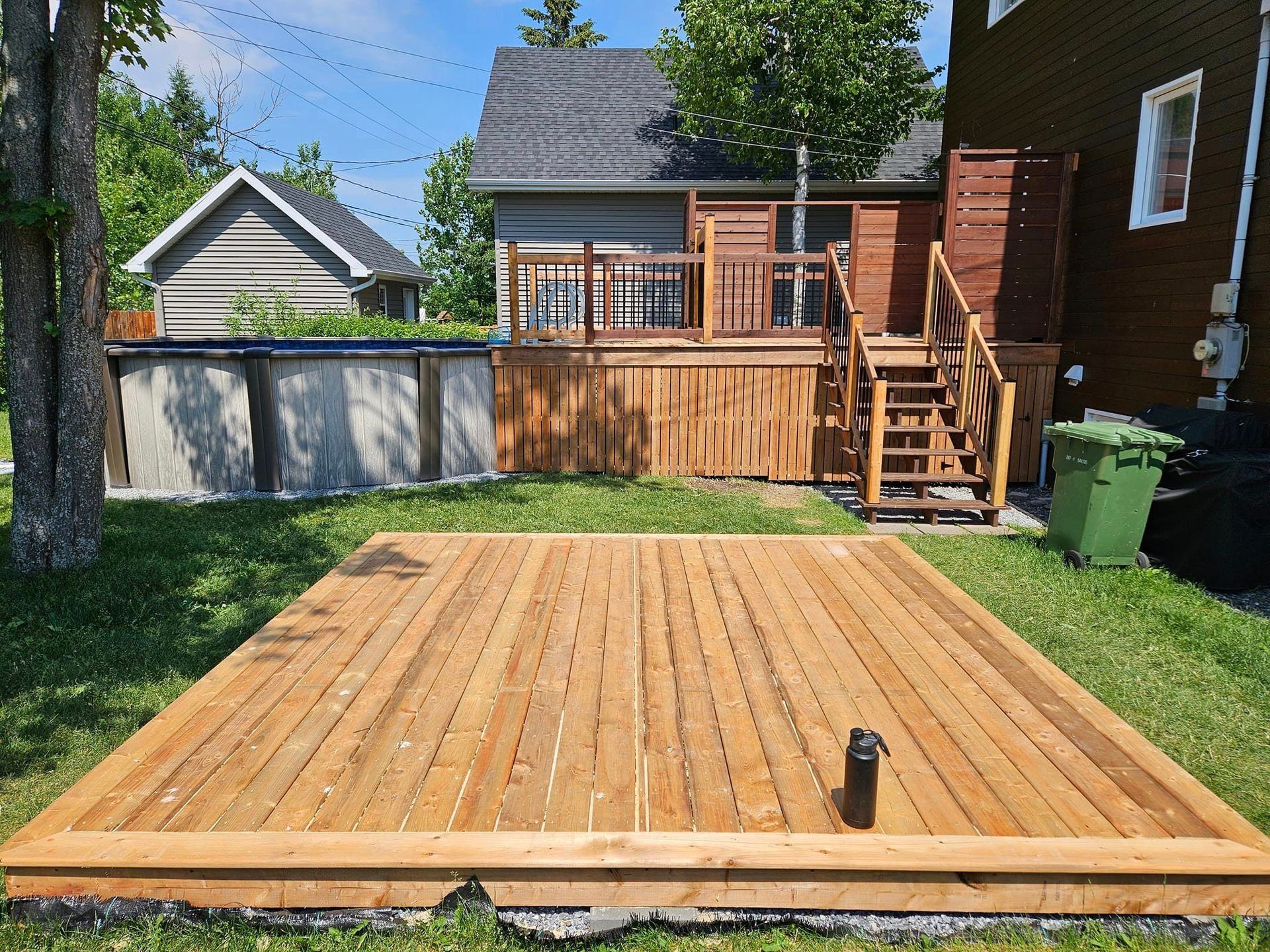 Une terrasse en bois est assise dans l'herbe devant une maison.