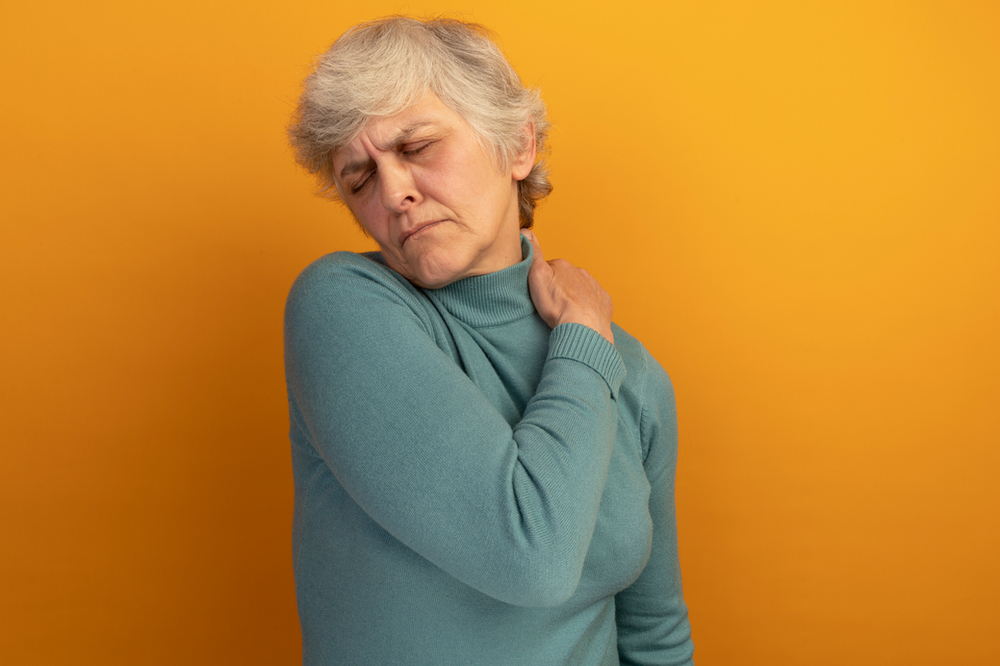 An elderly woman is holding her shoulder in pain.