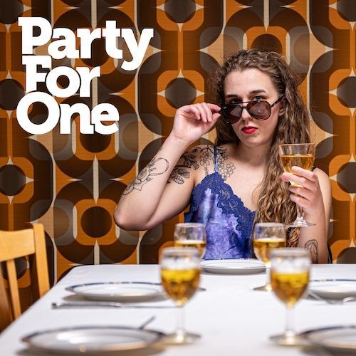 A woman is sitting at a table holding a glass of wine with the words party for one above her