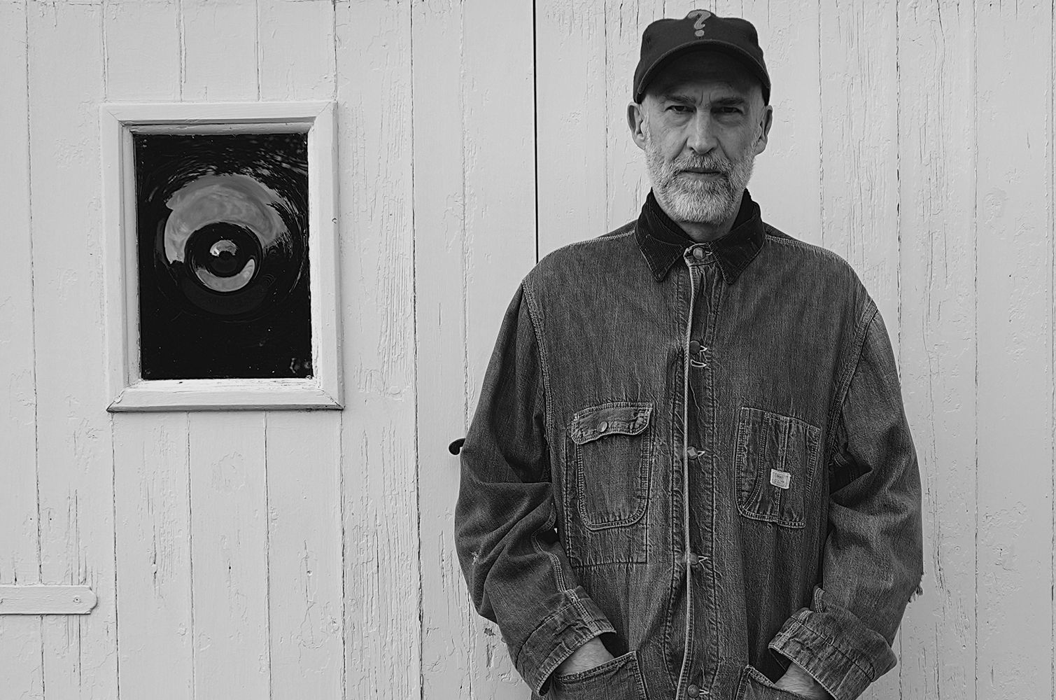 A black and white photo of a man standing in front of a white wall.