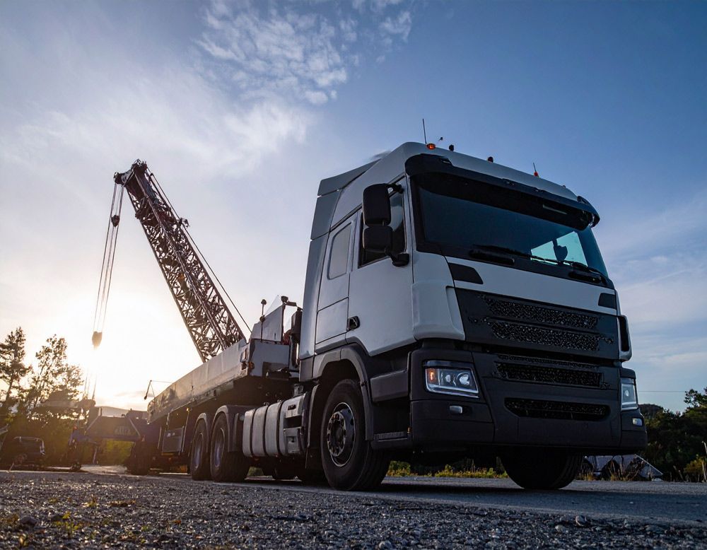 A white truck with a crane attached to it is parked on the side of the road.