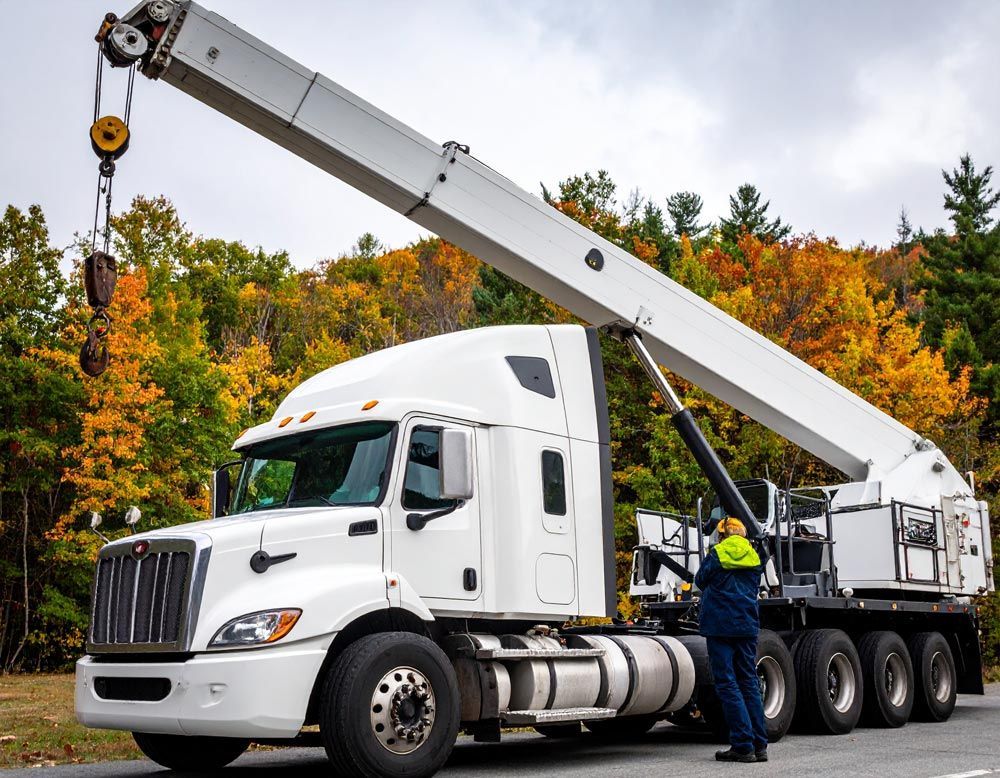 A man is standing next to a semi truck with a crane attached to it.