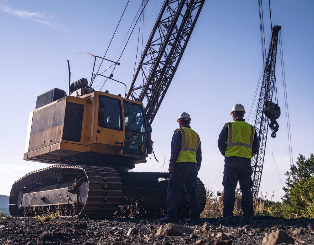Two construction workers are standing in front of a large crane.