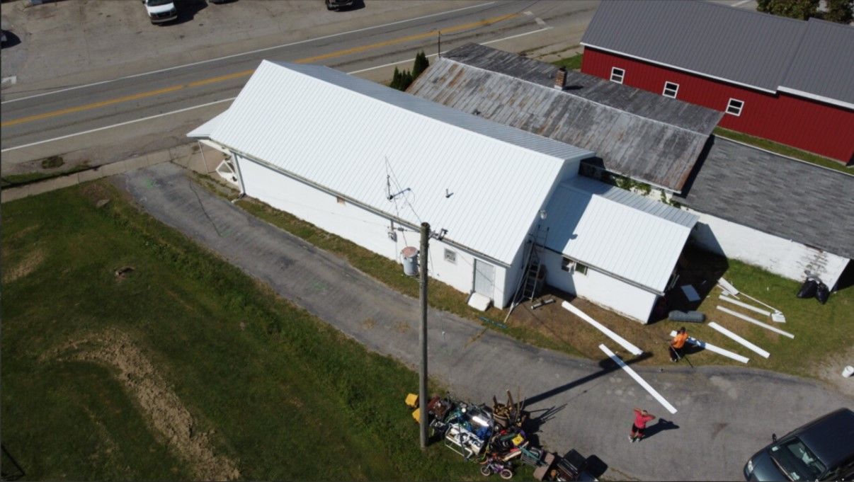 An aerial view of a white building with a red barn in the background.