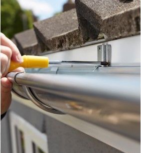A person is fixing a gutter with a yellow screwdriver.
