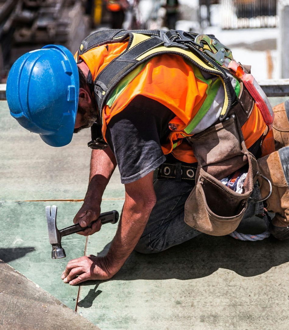A construction worker wearing a blue helmet is kneeling down holding a hammer