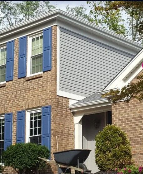 A brick house with blue shutters and a wheelbarrow in front of it