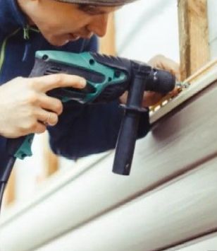 A construction worker wearing a blue helmet is kneeling down holding a hammer