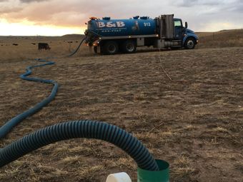 Blue water tanker truck in a dry field, with a hose stretched across the ground at sunset. Blue water tanker truck in a dry field, with a hose stretched across the ground at sunset.