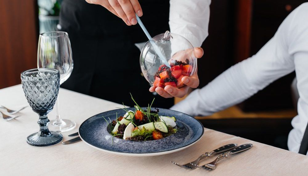 A man is pouring strawberries into a salad on a plate.