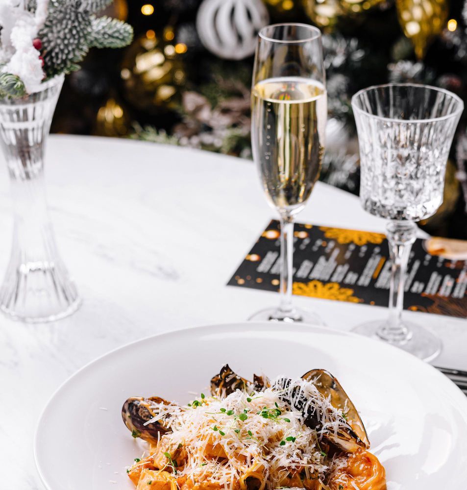 A plate of pasta with mushrooms and cheese next to a glass of champagne on a table.