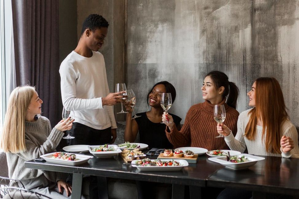 A group of people are sitting at a table eating food and drinking wine.