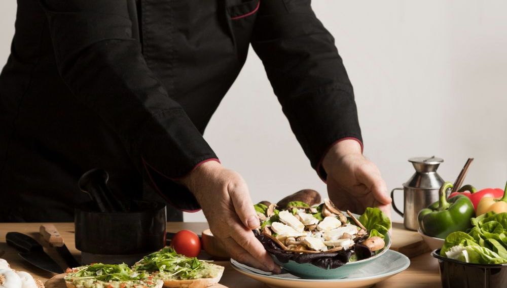 A chef is preparing a salad on a plate.