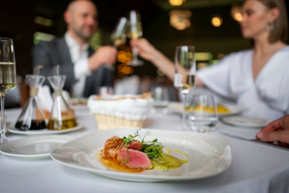 A close up of a plate of food on a table with people toasting in the background.