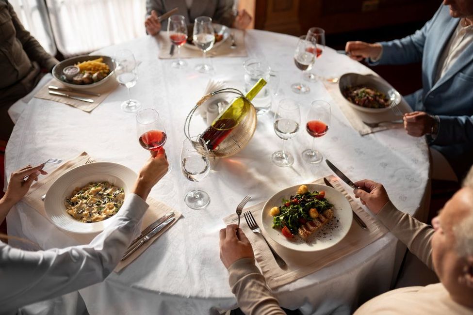 A group of people are sitting at a table eating food and drinking wine.