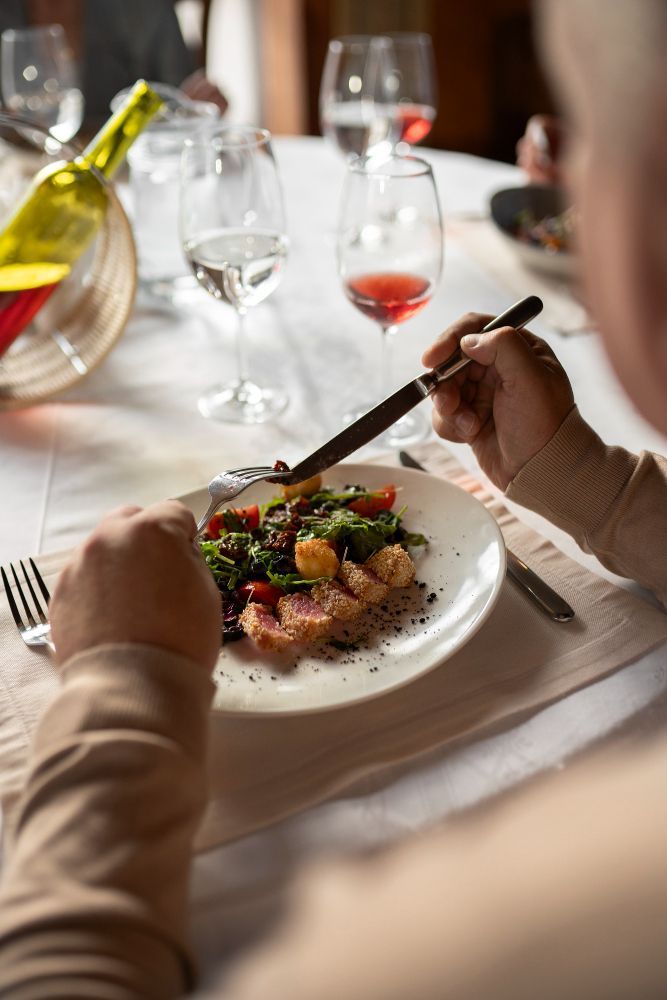 A man is sitting at a table eating a salad and drinking wine.