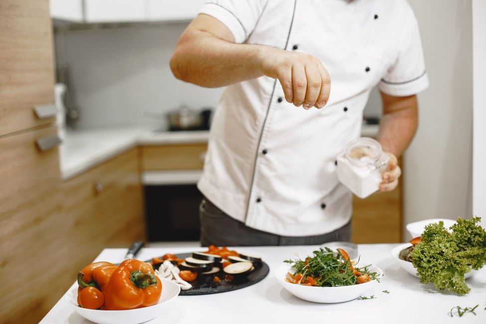 A man in a chef 's uniform is preparing food in a kitchen.