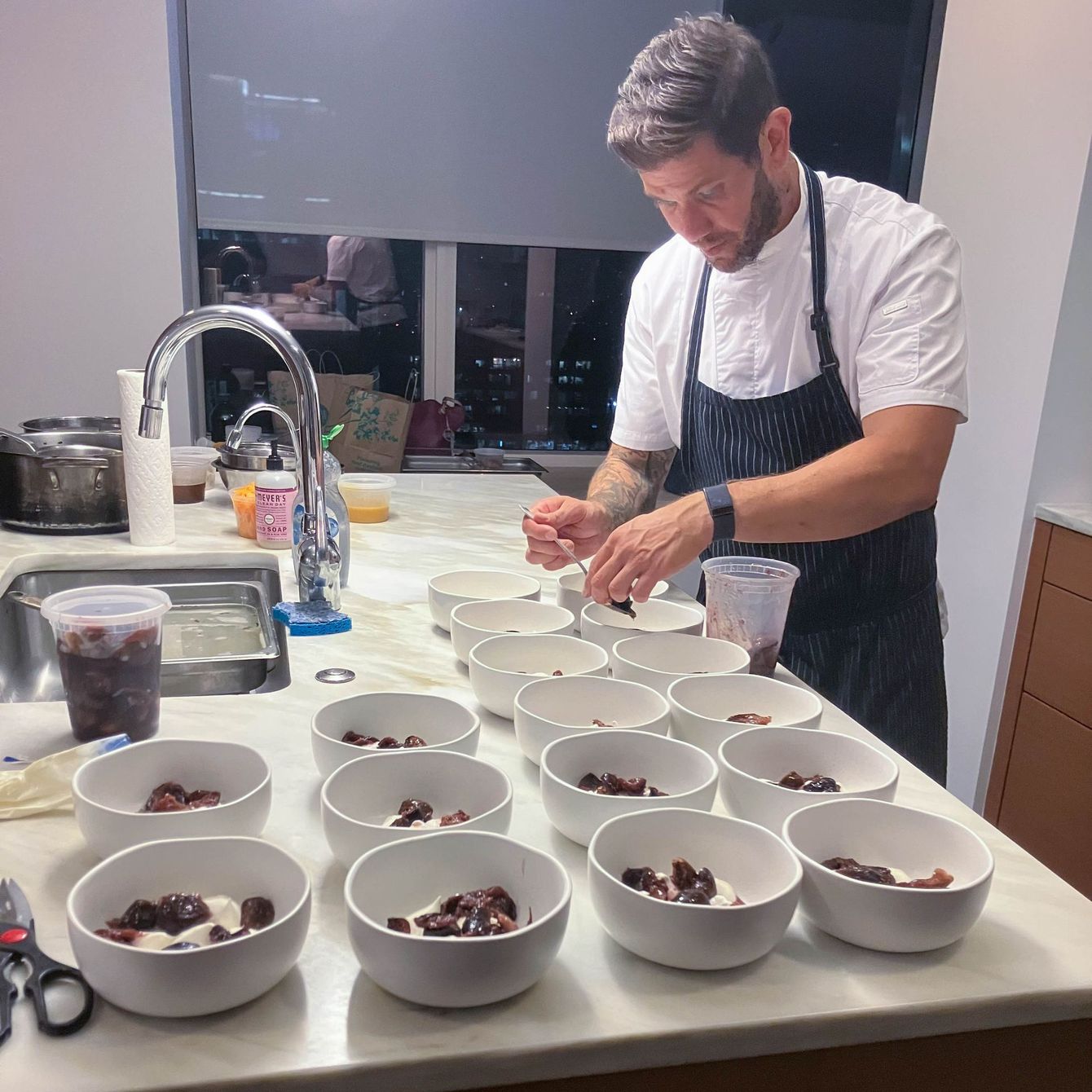 A man in an apron is preparing food in bowls on a counter