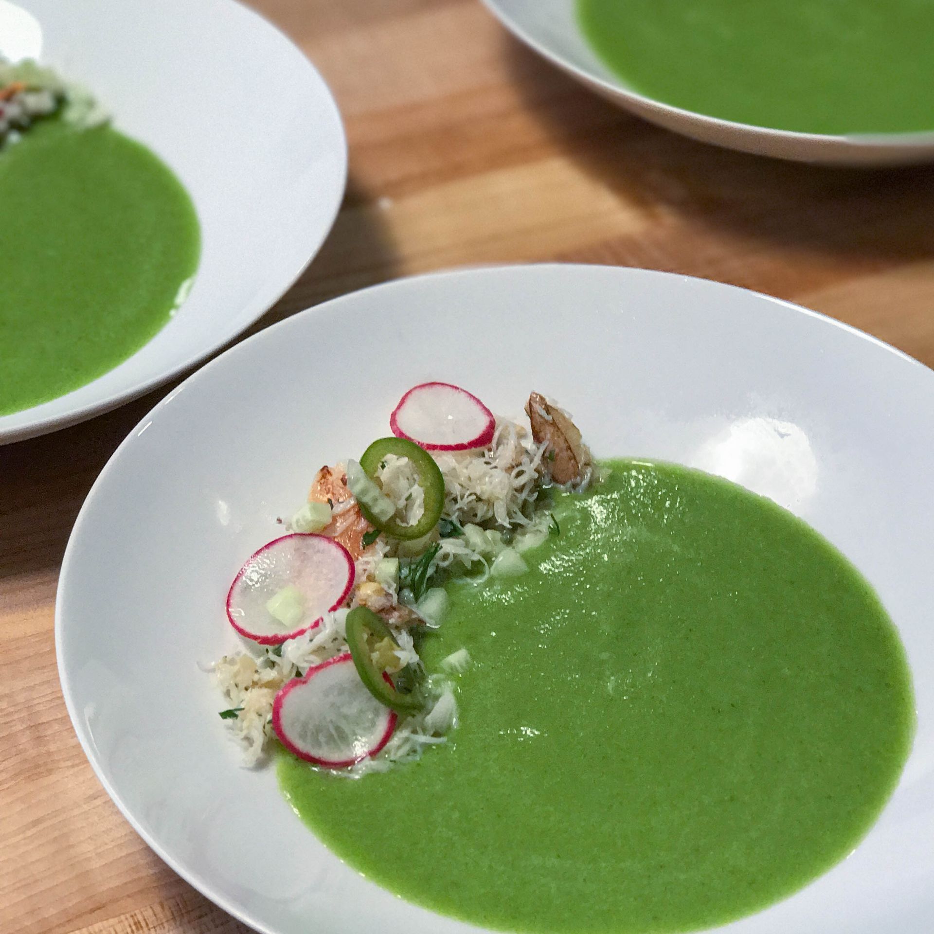 Two bowls of green soup with vegetables on a wooden table