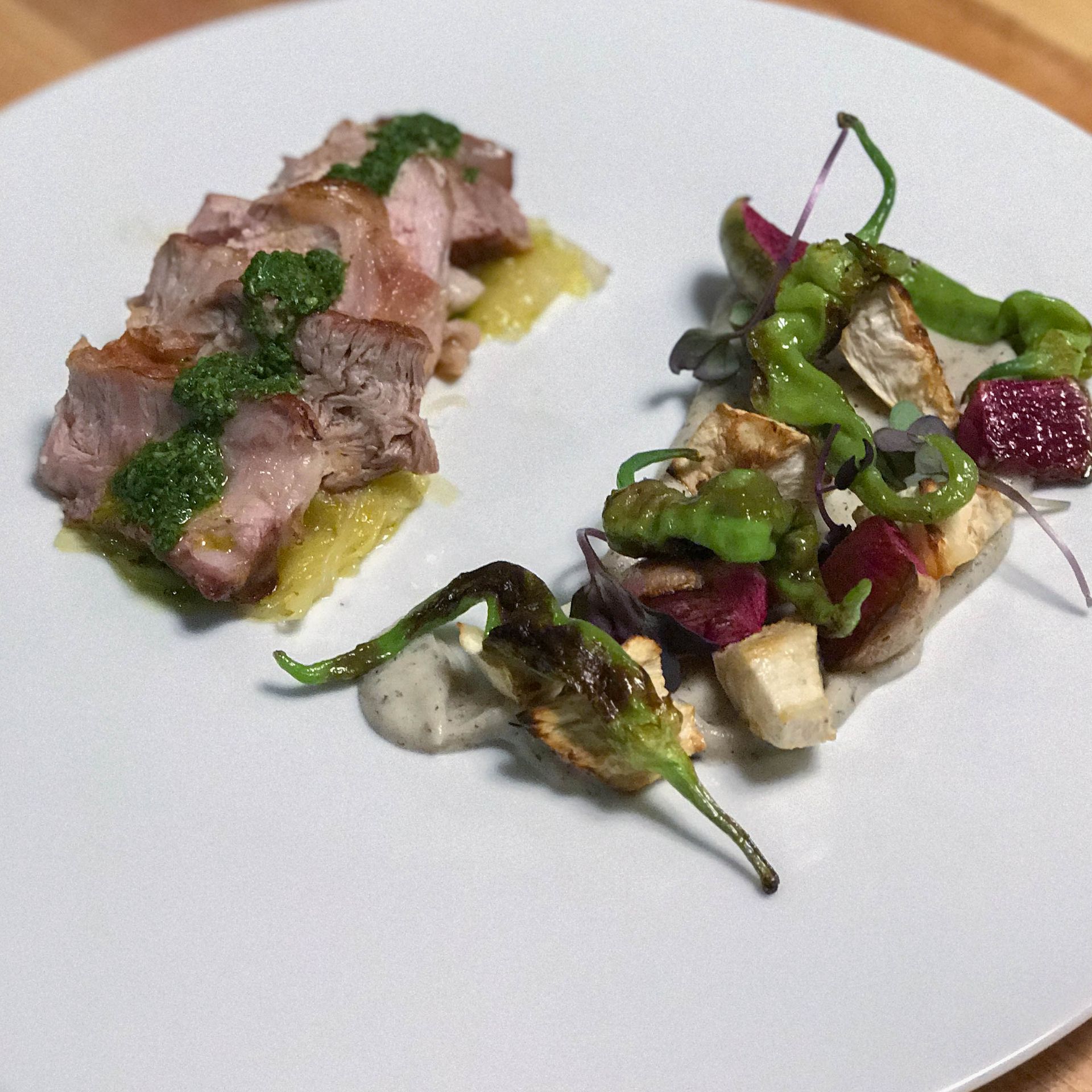 A white plate topped with meat and vegetables on a wooden table