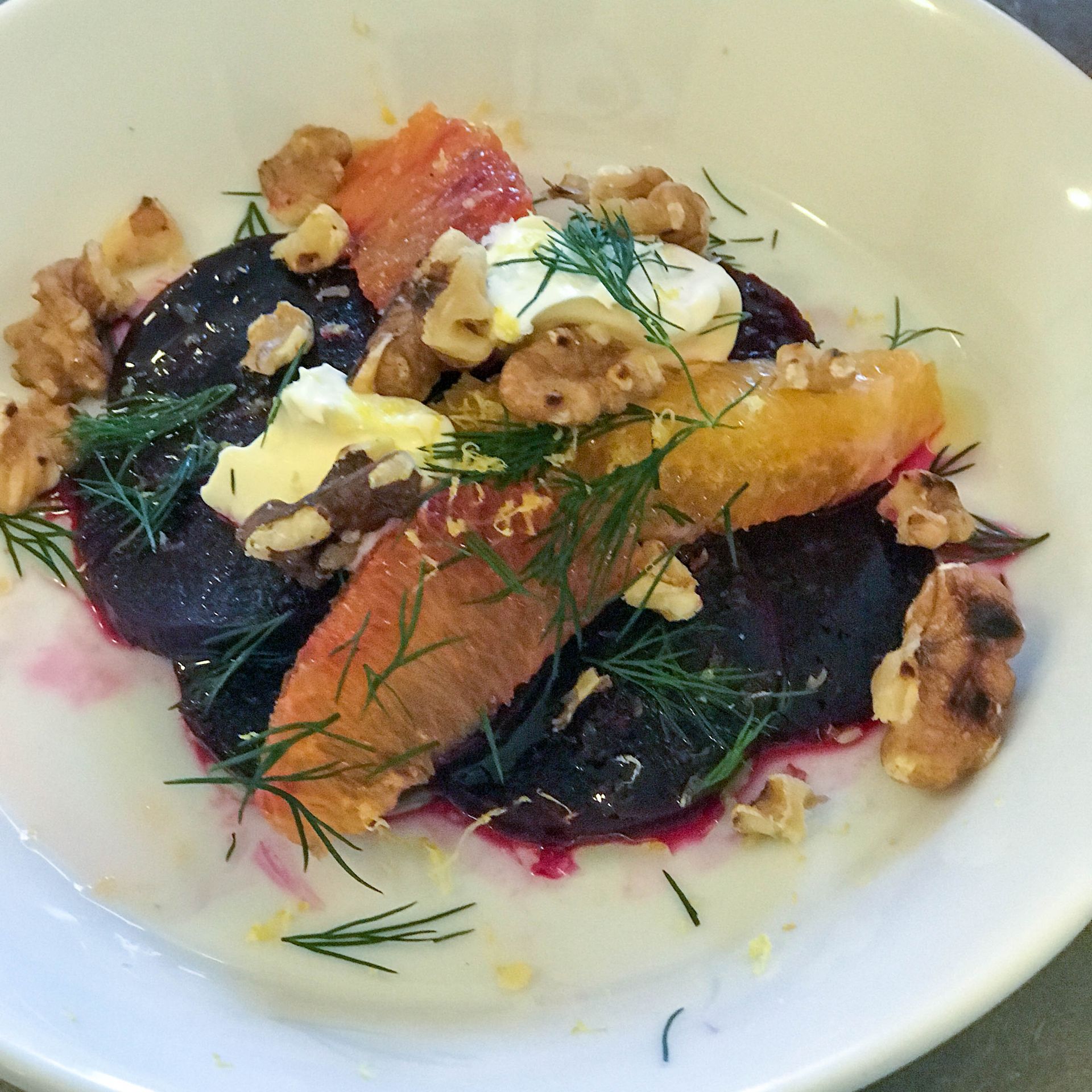 A white plate topped with a salad of beets oranges and walnuts