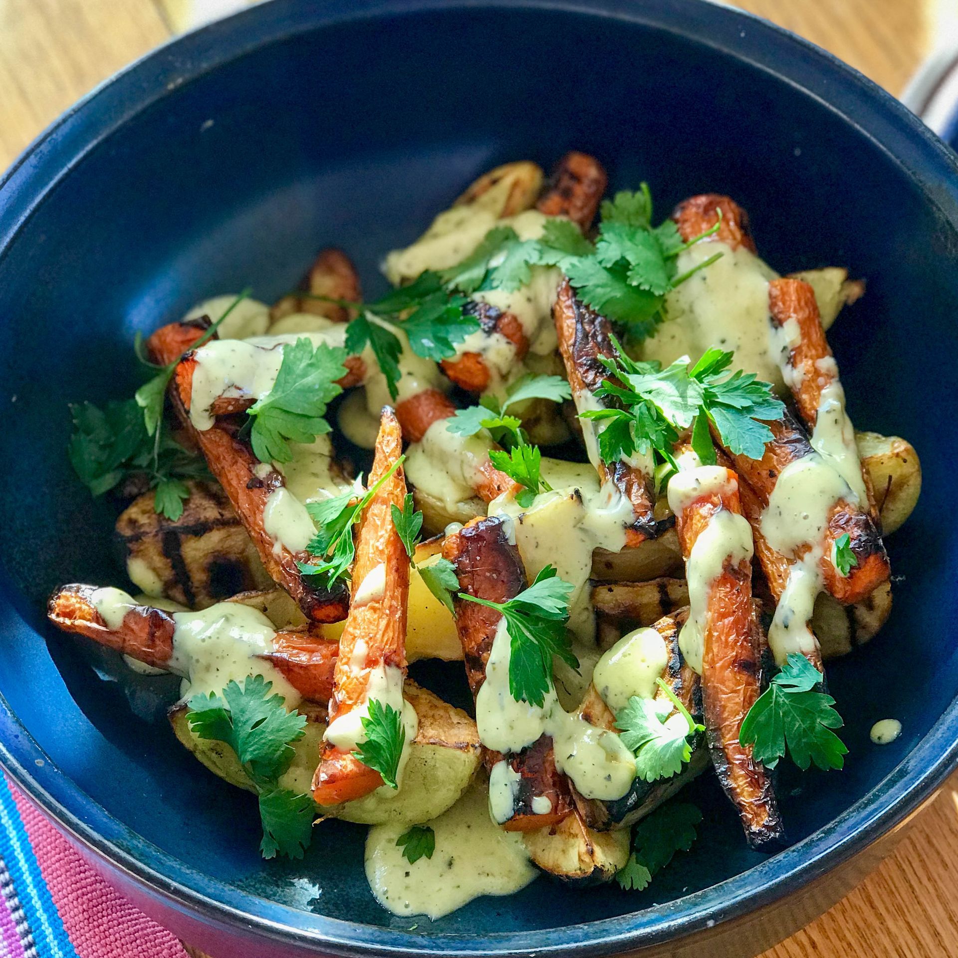 A bowl of carrots and potatoes with sauce and parsley