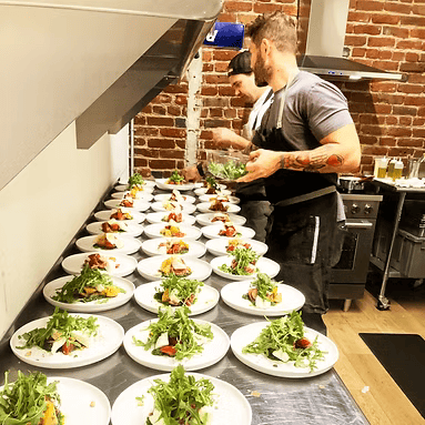 Two men are preparing plates of food in a kitchen.