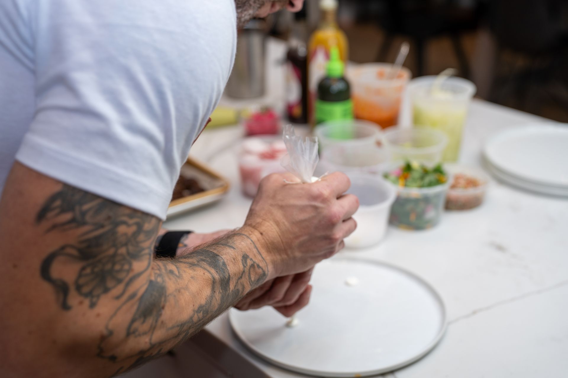 A man with tattoos on his arm is preparing food on a plate.