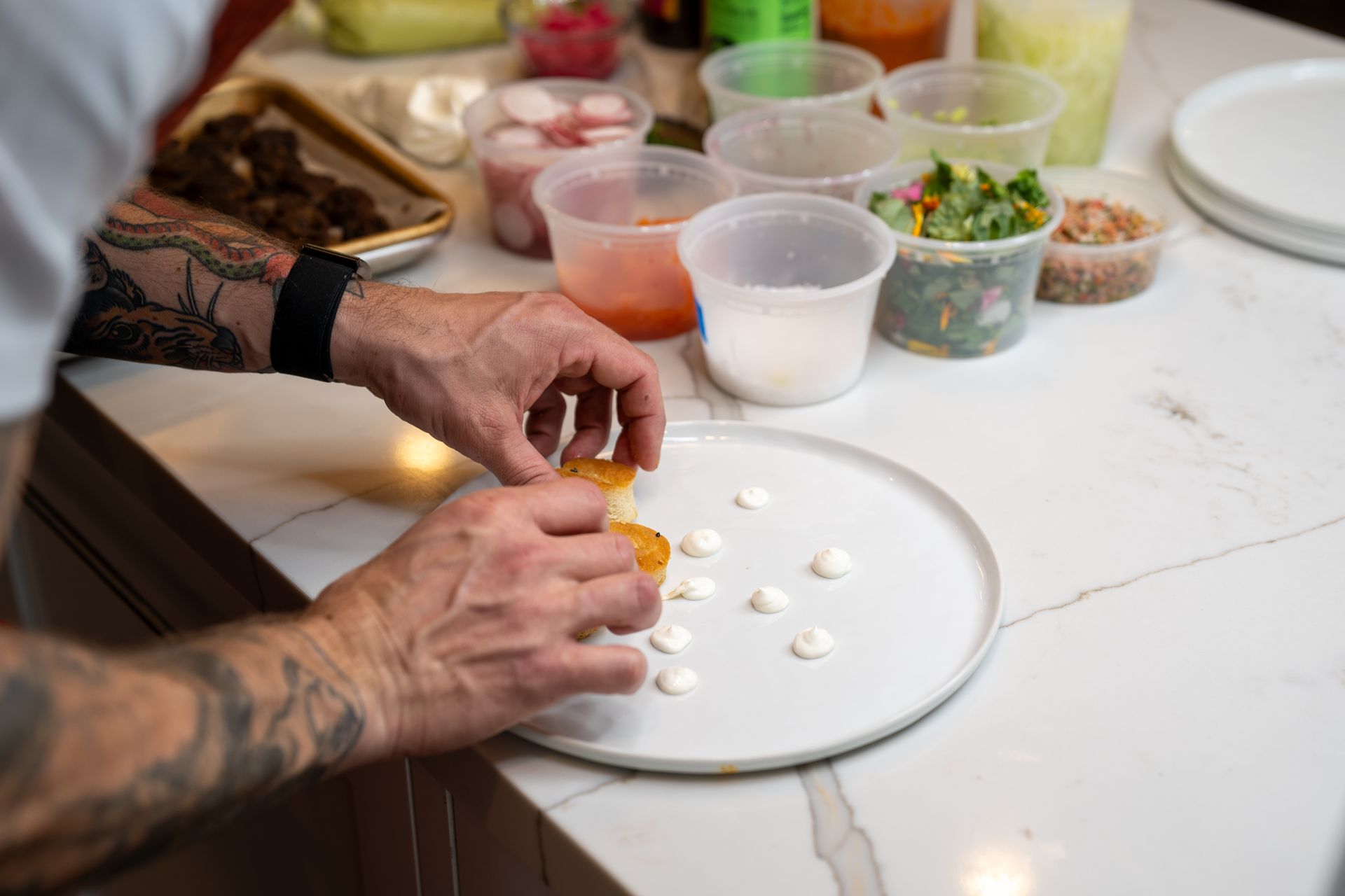 A man is preparing food on a white plate on a counter.