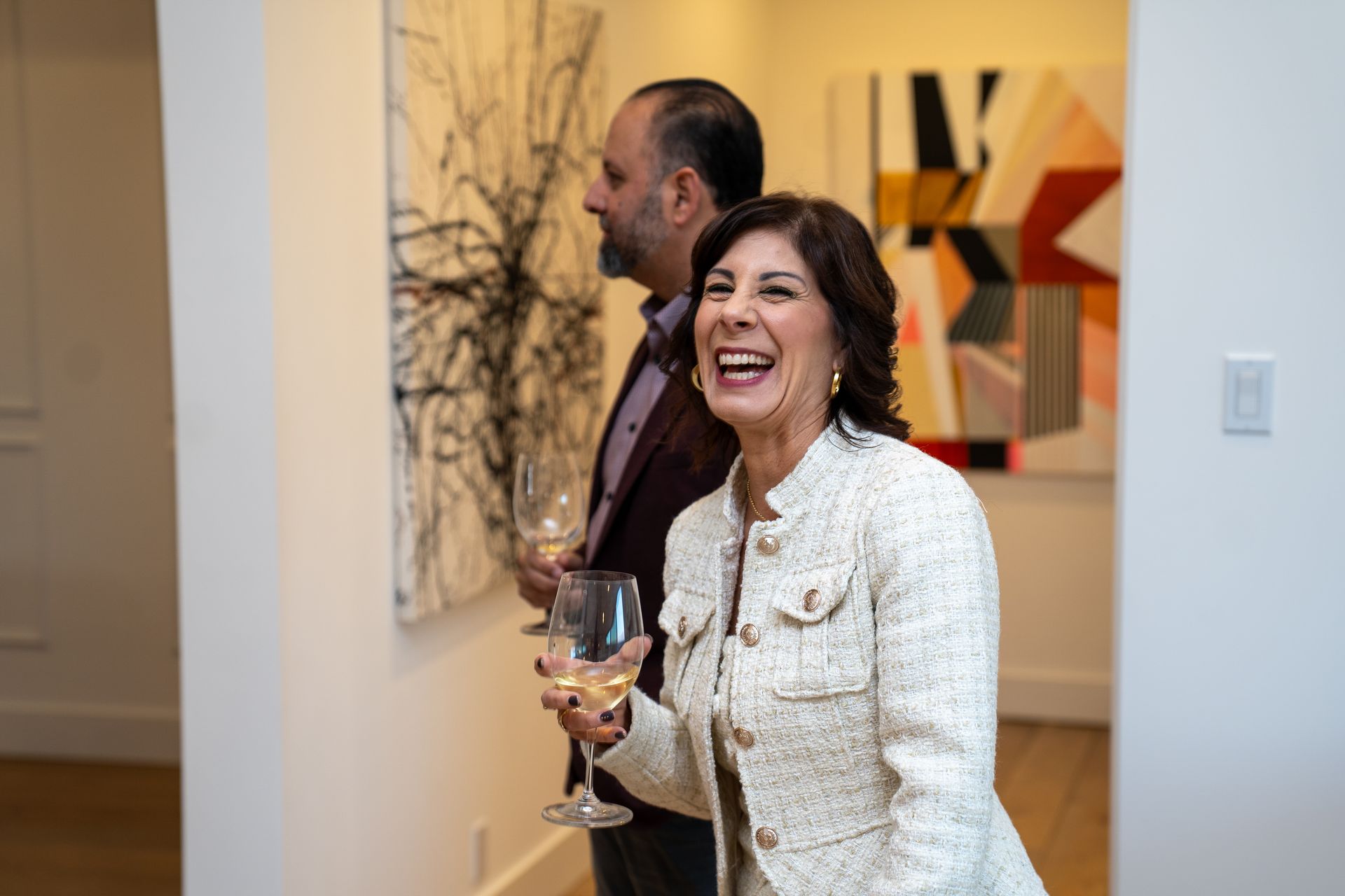 A man and a woman are standing next to each other in a room holding wine glasses.