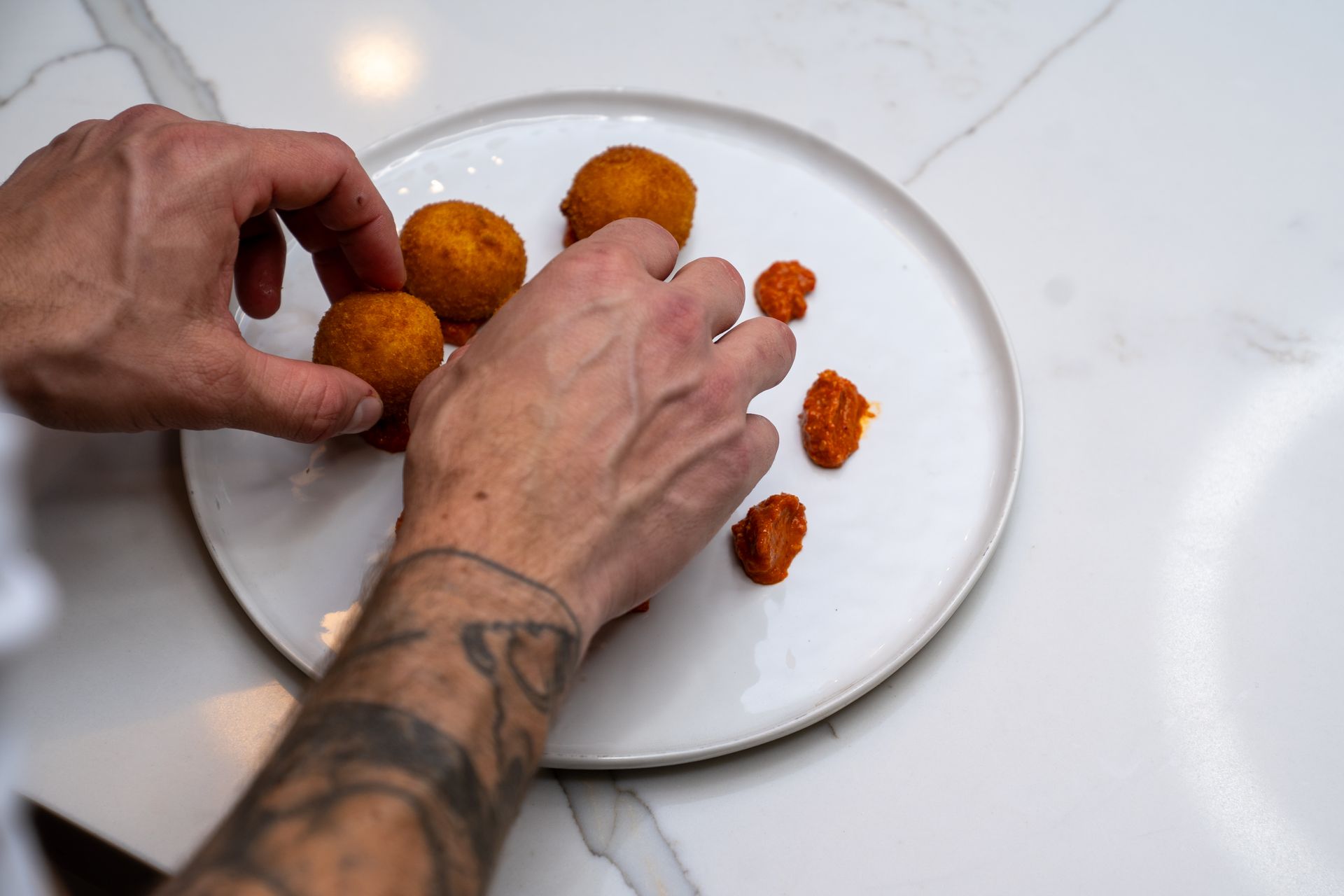 A person with a tattoo on their arm is putting food on a plate.