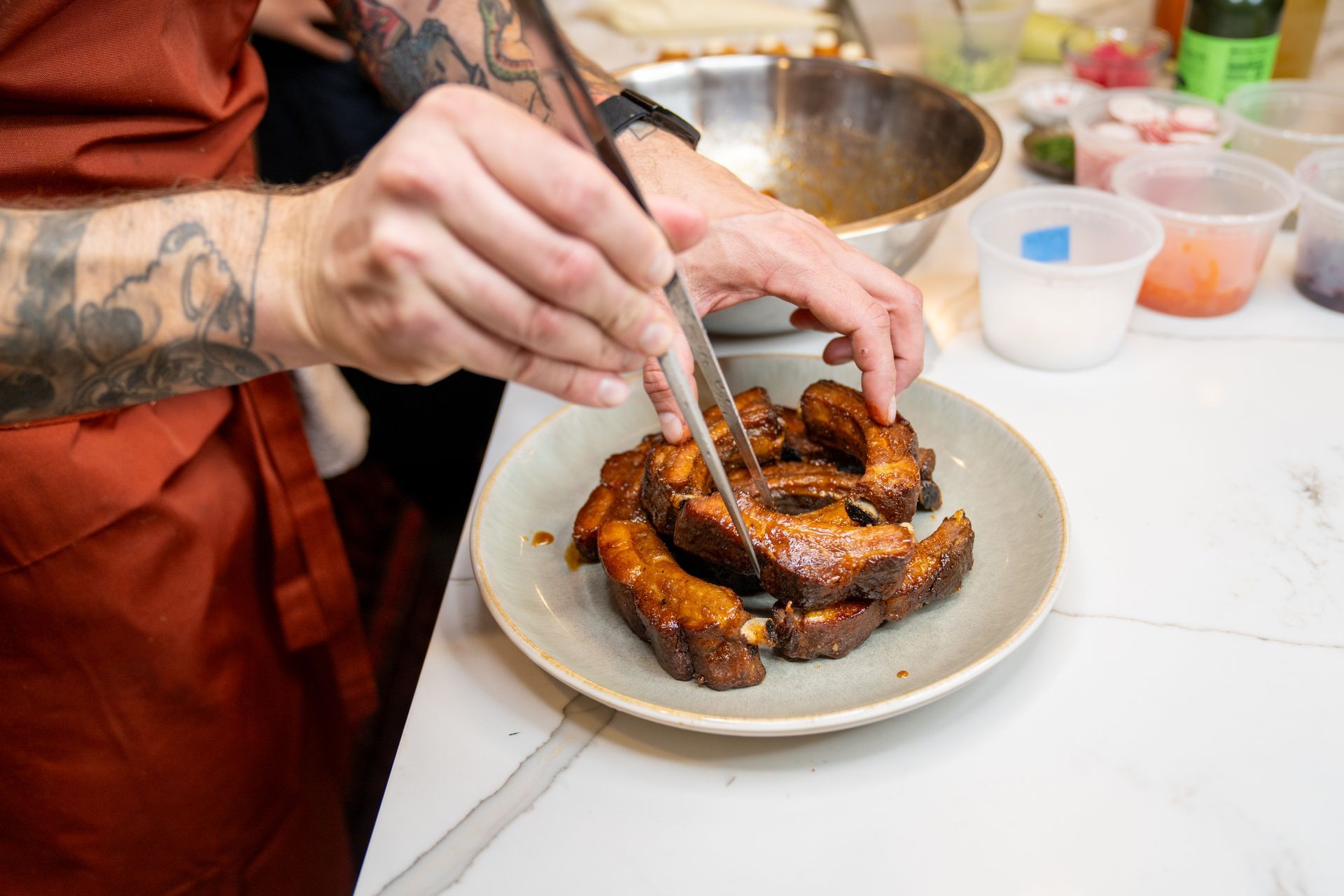 A person is cooking ribs on a plate with tongs.