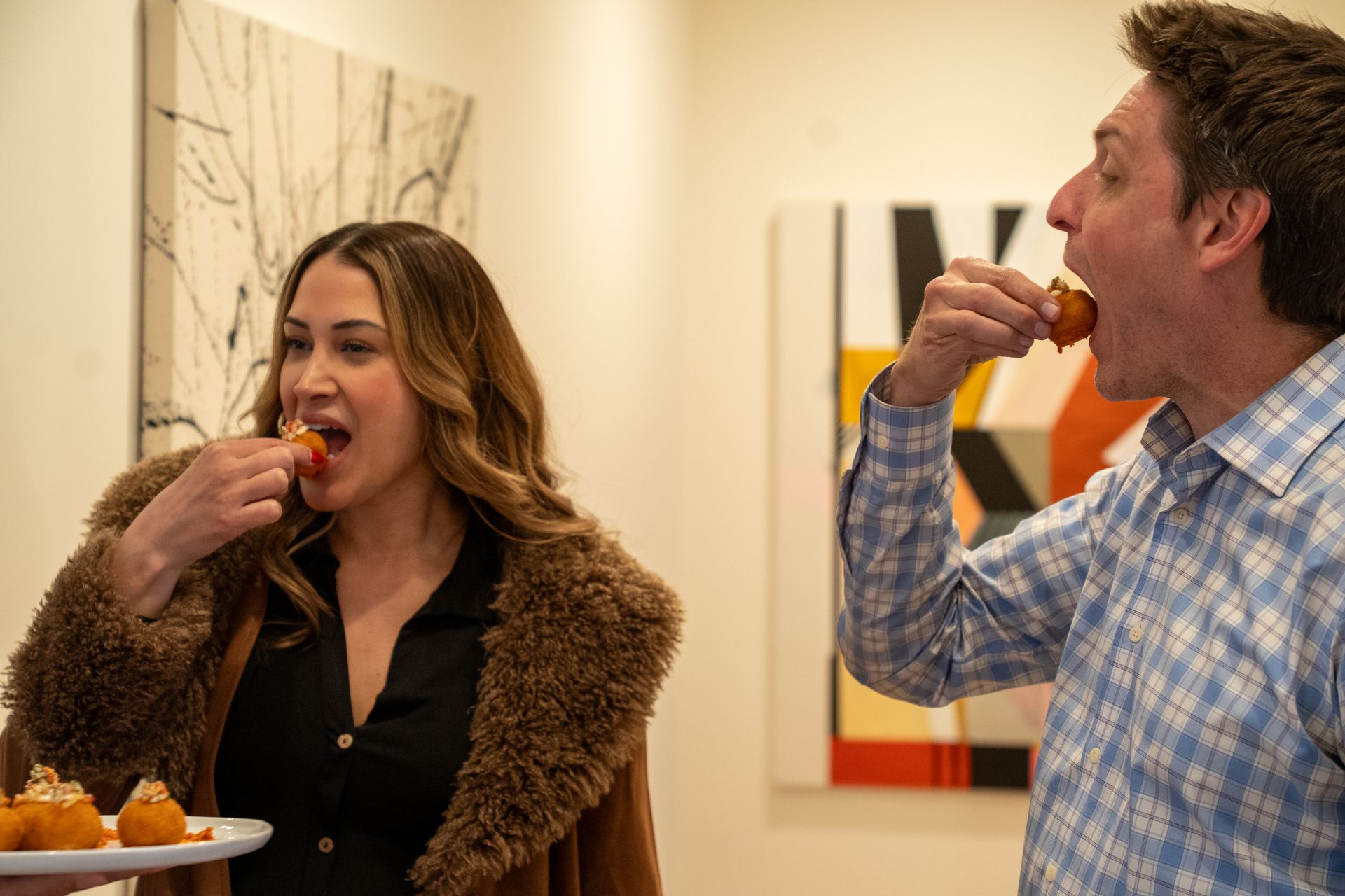 A man and a woman are eating food in a room.
