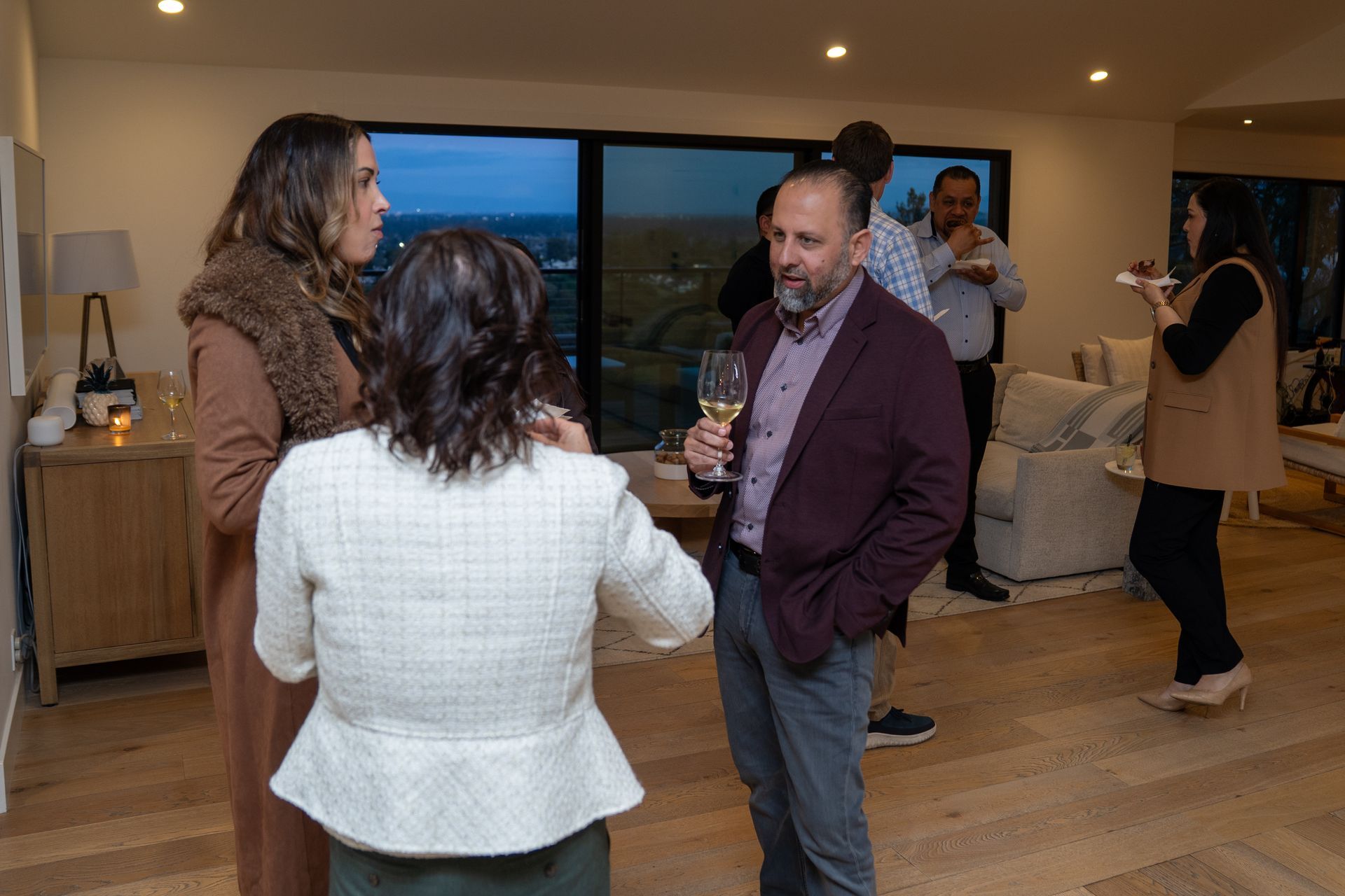 A group of people are standing in a living room talking to each other.